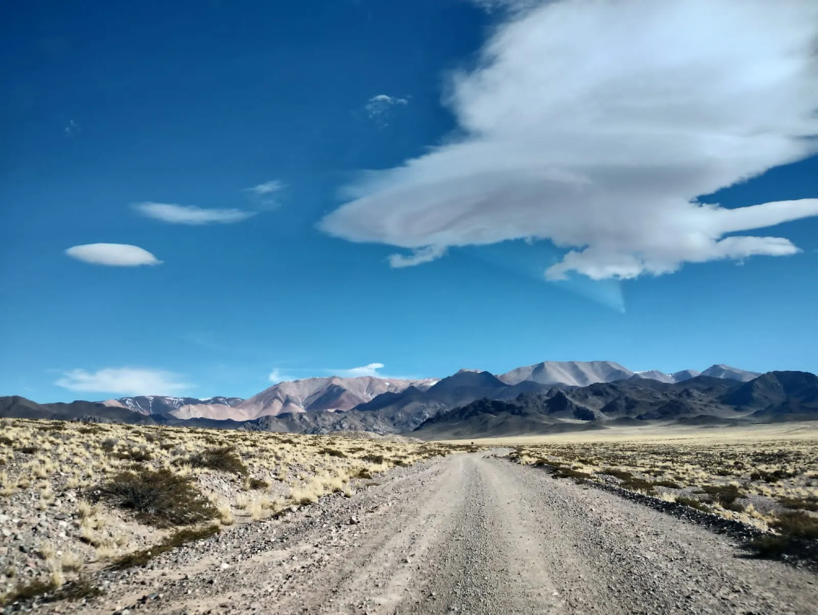 Camino de ripio hacia la cordillera bajo un cielo azul con nubes