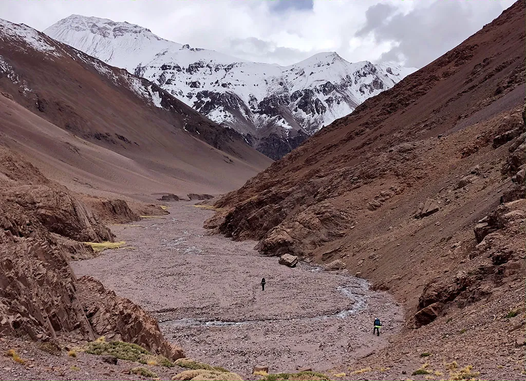 Montañistas recorriendo una quebrada rodeada de cumbres nevadas en Agua Negra