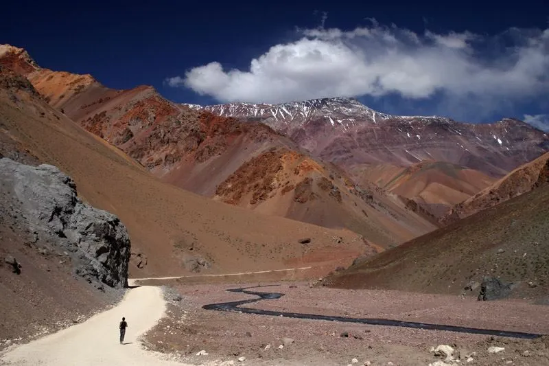 Montañista caminando junto a un arroyo entre montañas coloridas de Agua Negra